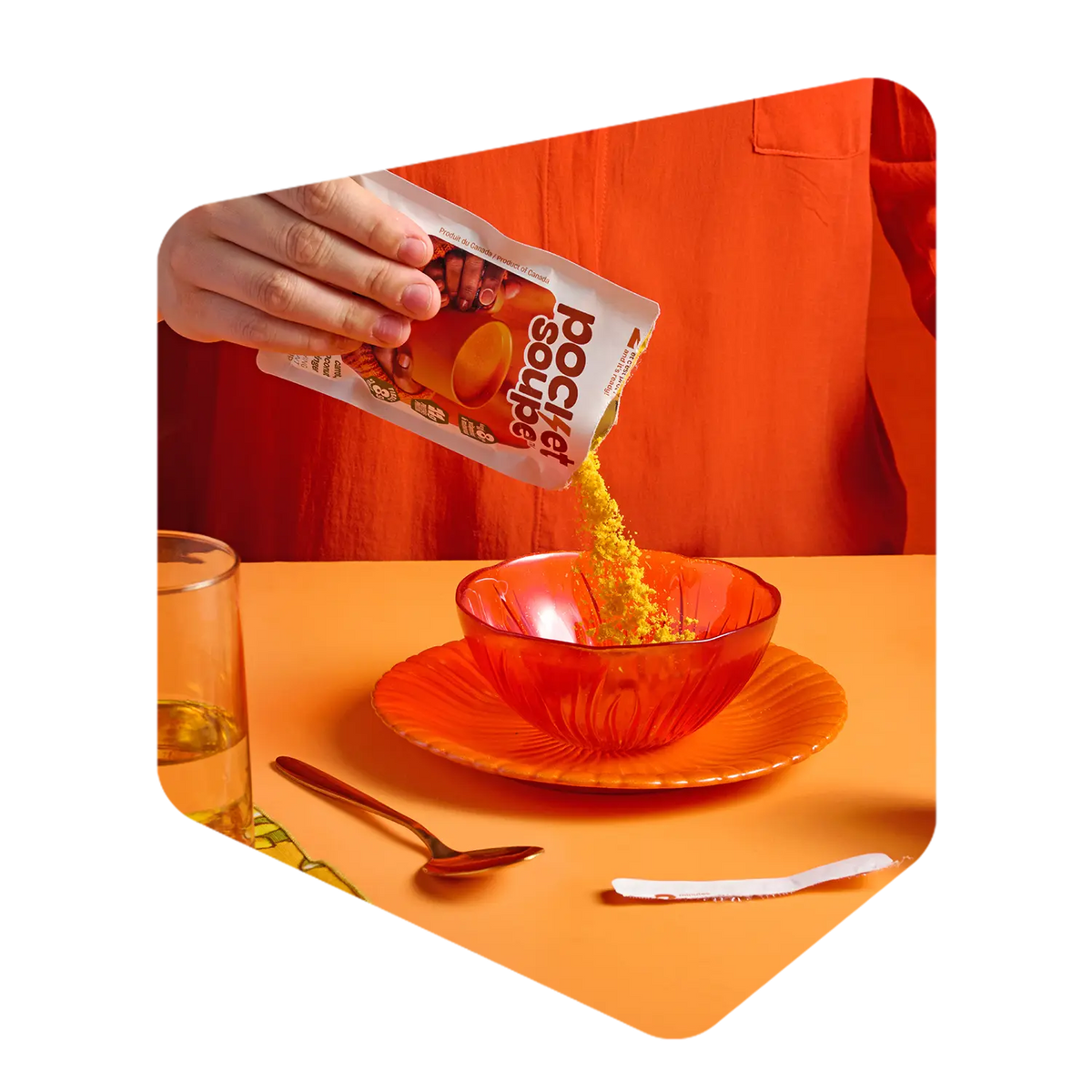 Poudre de soupe Pocket Soupe versée d'un sachet dans un bol de verre orange, sur une table dressée avec cuillère et verre d'eau