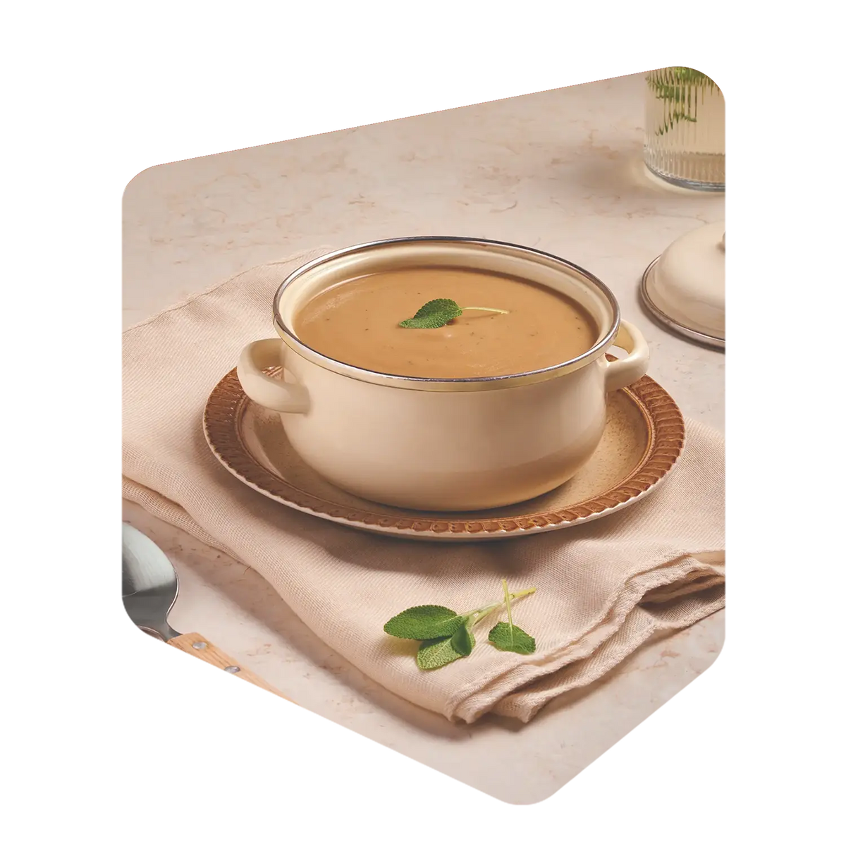 Bol de velouté aux oignons caramélisés Pocket Soupe garni d'une feuille de sauge, servi sur une nappe beige