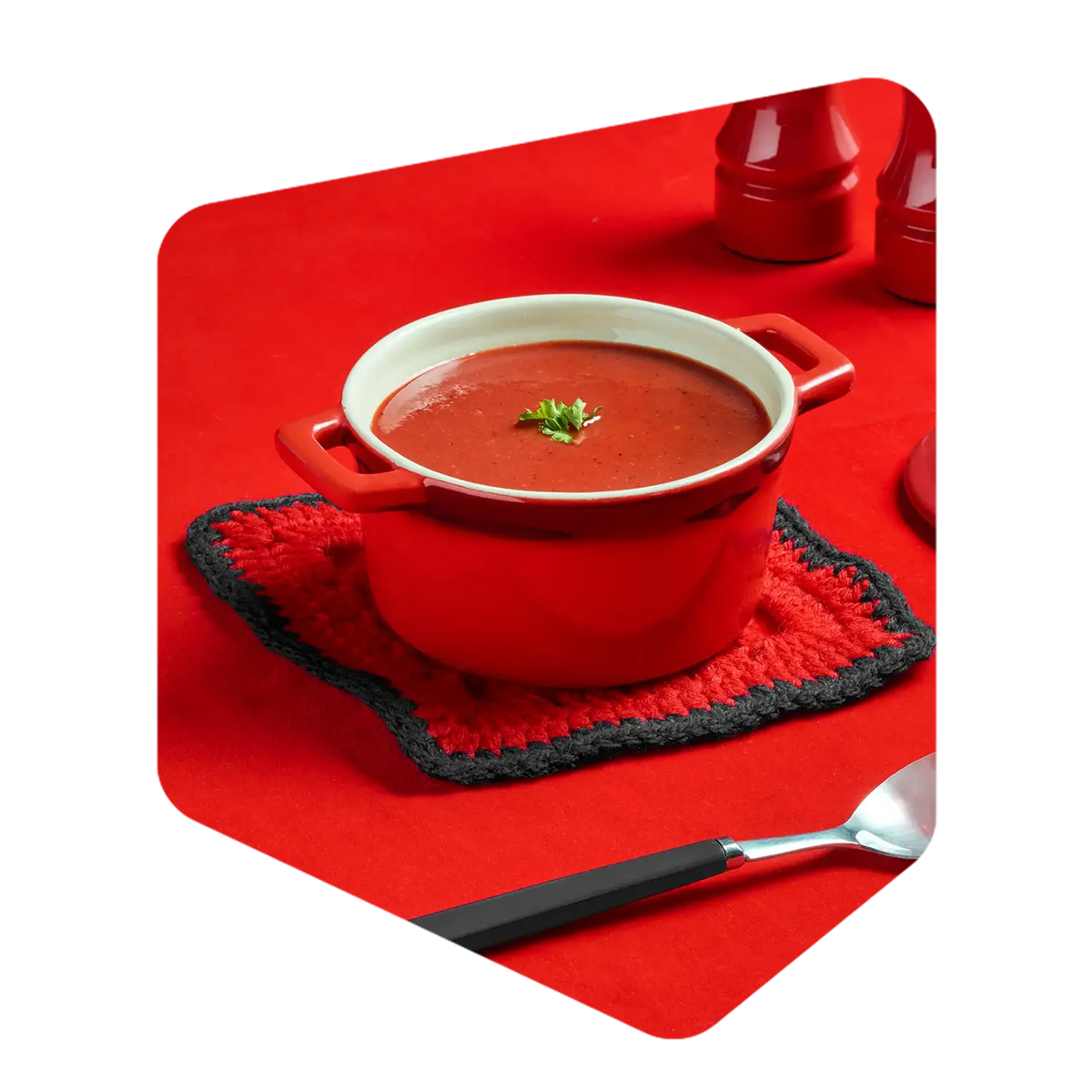 Cocotte rouge remplie de soupe aux tomates Pocket Soupe garnie de persil, posée sur un carré de laine tricoté