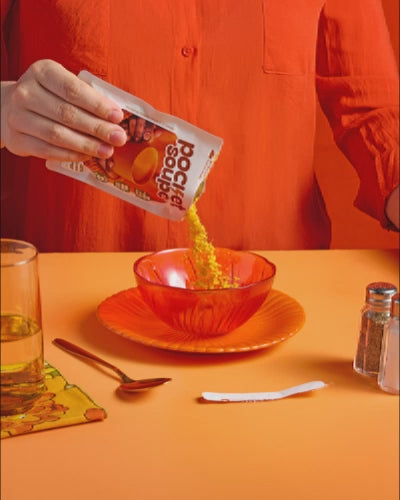 Animation en stop motion : la poudre d'un sachet Pocket Soupe carotte, coco et gingembre est versée dans un bol de verre orangé, sur une table dressée avec une cuillère et un verre d'eau.